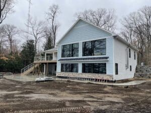 exterior of large, multi-room addition on lakeshore with blue siding, black windows, and composite deck