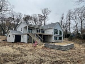 exterior of large, multi-room addition on lakeshore with blue siding, black windows, and composite deck