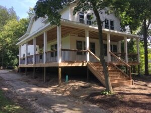 Wrap around porch with wood decking, railings and soffit on home with white siding
