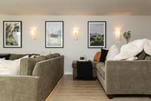 finished basement remodel with wall sconce lights, green couches, and vinyl plank flooring