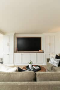 wall with white cabinets around a framed TV with green couch in foreground