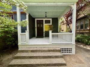 finished front porch restoration on historic home. concrete steps leading up to white porch with cedar railings