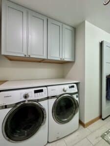 a white washer and drier with mint cabinets above them with gold hardware