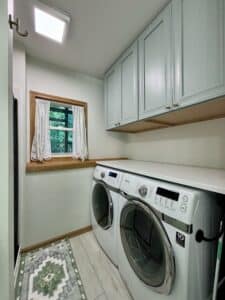 white washer and drier with mint cabinets above them with gold hardware and a window
