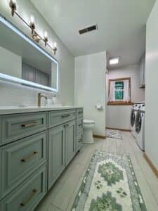 Full view of bathroom and laundry room remodel with tile floor, vanity cabinets, mirror, LED lights, washer and drier