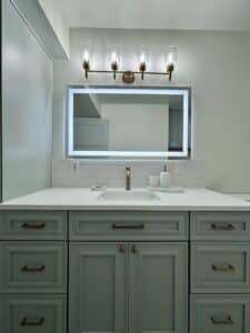Mint colored vanity cabinets with quartz countertop and tile backsplash. LED mirror and vanity lights above