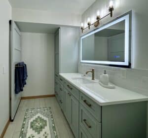 Vanity and pantry cabinets with quartz countertop, tile backsplash, smart mirror, tile flooring, and vanity light