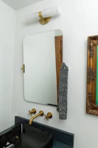 Small bathroom with black stone countertop, wall-mounted mirror, and brass fixtures