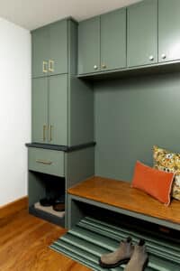 Custom mudroom built-in with green painted cabinetry, wood bench seat, overhead storage cabinets, brass hardware, and integrated seating area
