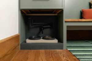 Custom mudroom built-in with green painted cabinetry, wood bench seat, brass hardware, and pet feeding station with faucet