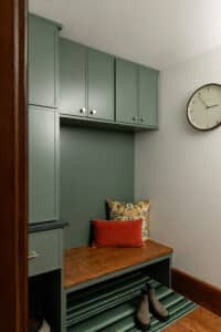 Custom mudroom built-in with green painted cabinetry, wood bench seat, overhead storage cabinets, brass hardware, and integrated seating area