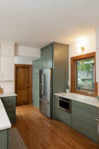 Kitchen remodel with sage cabinets, white stone countertops, stainless steel appliances, hardwood floors and stained wood trim