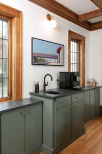 Built-in coffee bar with sink, espresso maker, black stone countertops on sage green cabinets with brass hardware