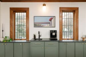 Built-in coffee bar with sink, espresso maker, black stone countertops on sage green cabinets with brass hardware